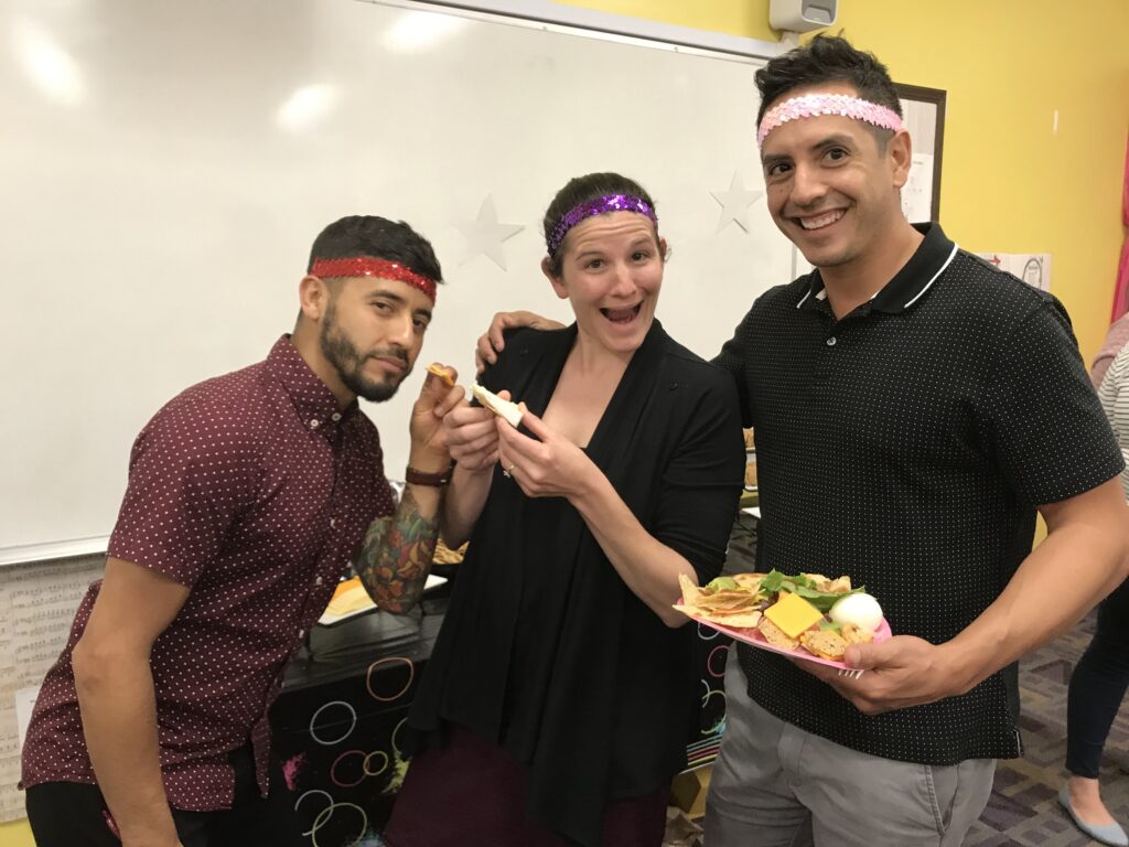  Three people are posing for a photo, wearing party headbands, with snacks in hand, and a whiteboard in the background.