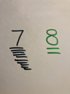 Pad of paper with the number 7 written in black and the number 8 in green, with lines under each number